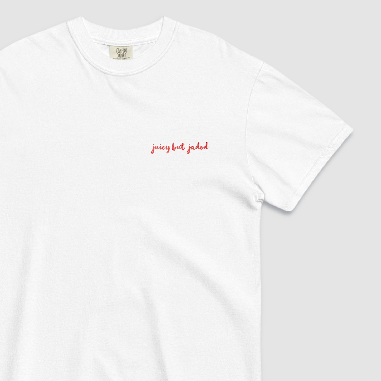 Close up of a white tshirt with 'juicy but jaded' text written on the left chest in red